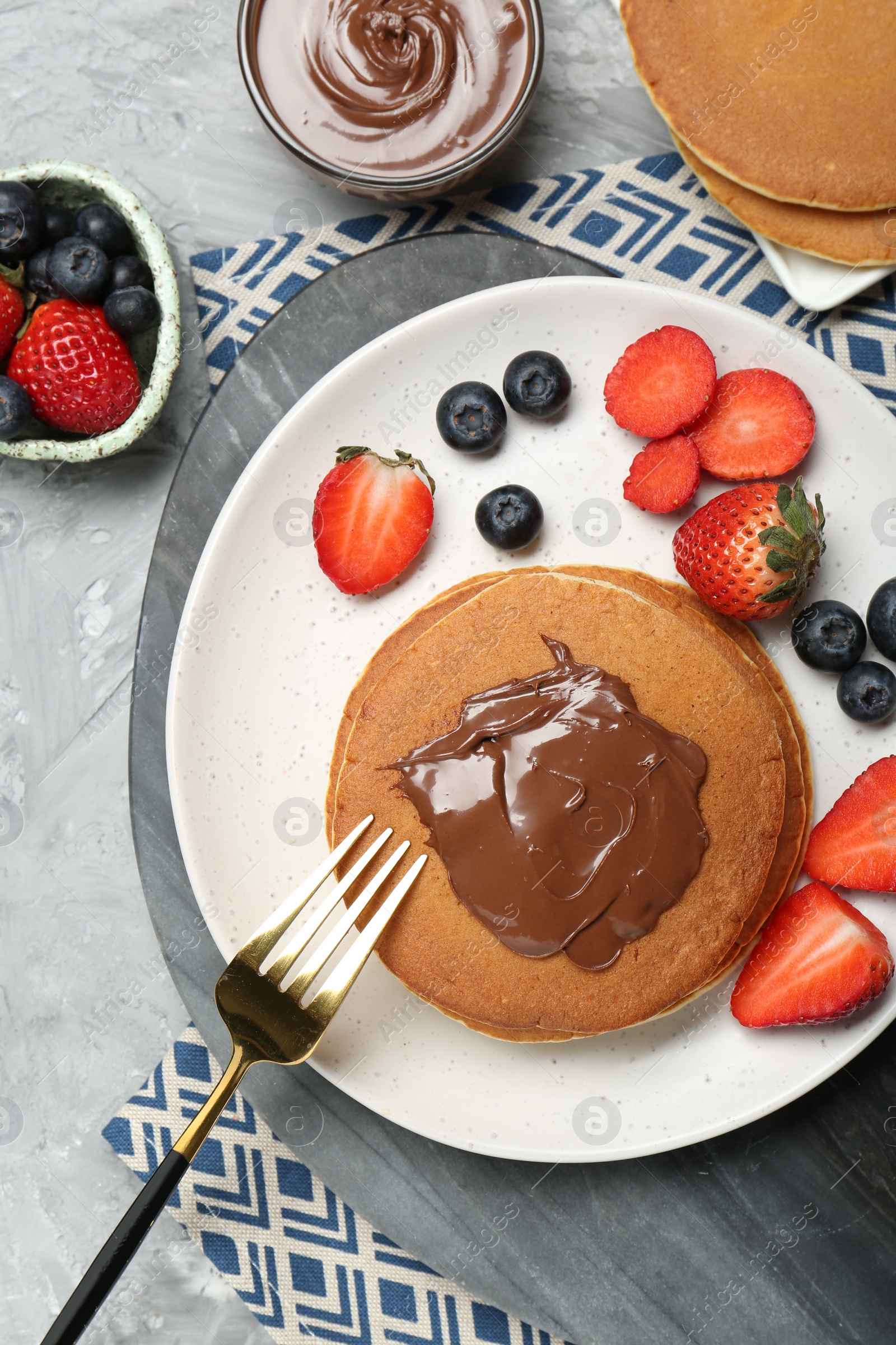 Photo of Tasty pancakes with chocolate paste and berries on grey table, flat lay