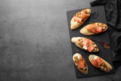 Photo of Slate plate with tasty bruschettas on grey table. Space for text