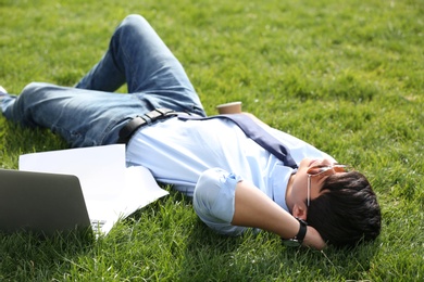 Young man lying on green lawn in park. Joy in moment