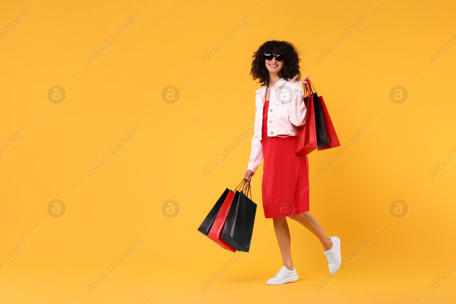 Photo of Happy young woman with shopping bags and stylish sunglasses on yellow background. Space for text