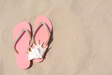 Photo of Stylish pink flip flops and seashell on sandy beach, flat lay. Space for text