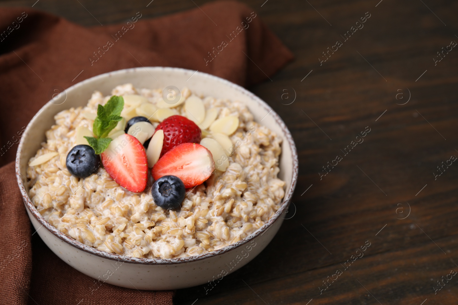 Photo of Tasty oatmeal with strawberries, blueberries and almond flakes in bowl on wooden table. Space for text