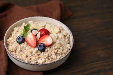 Tasty oatmeal with strawberries, blueberries and almond flakes in bowl on wooden table. Space for text