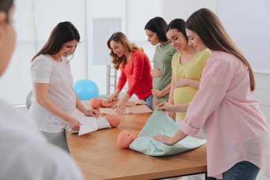 Photo of Pregnant women learning how to swaddle baby at courses for expectant mothers indoors