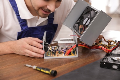 Photo of Male technician repairing power supply unit at table, closeup