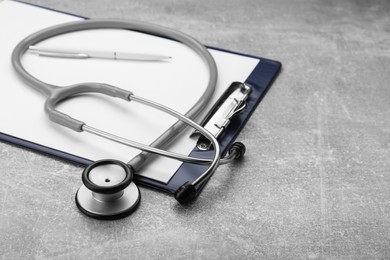 Photo of Clipboard with stethoscope on grey table, closeup. Space for text