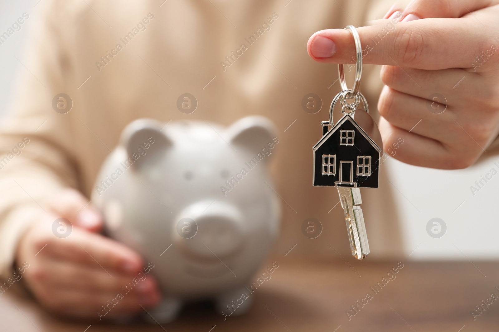 Photo of Man holding key and piggy bank at wooden table, closeup. Space for text. Saving money concept