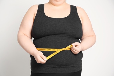 Photo of Overweight woman with measuring tape on light background