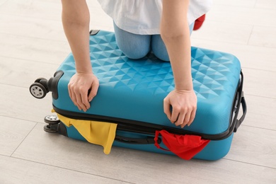Photo of Young woman struggling to close suitcase indoors