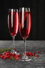 Photo of Tasty cranberry cocktail with rosemary in glasses on gray textured table against dark background