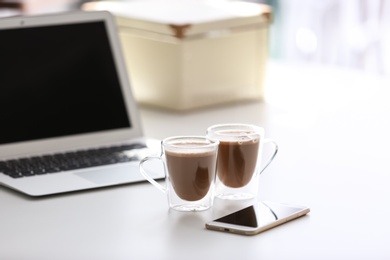 Cups of coffee, mobile phone and laptop on table