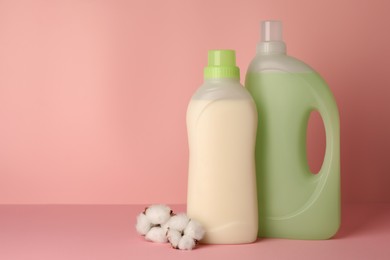 Photo of Bottles of fabric softener and fluffy cotton flowers on pink background, space for text