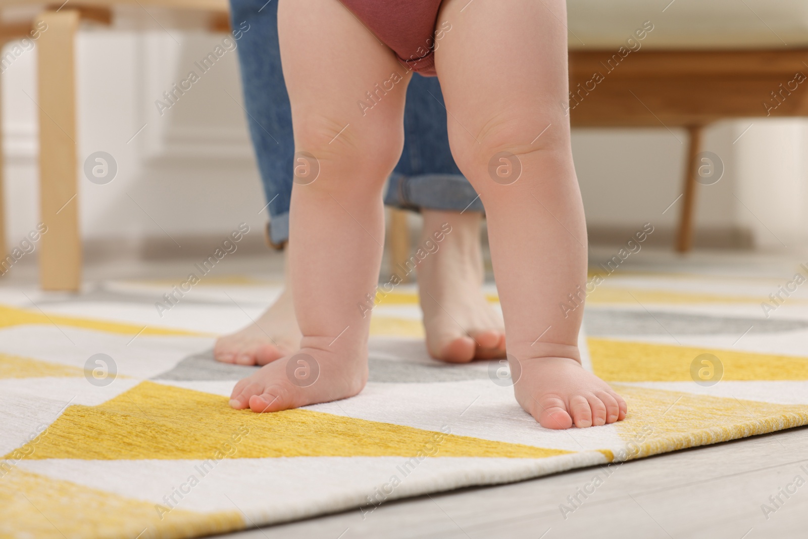 Photo of Mother supporting her baby son while he learning to walk on carpet at home, closeup