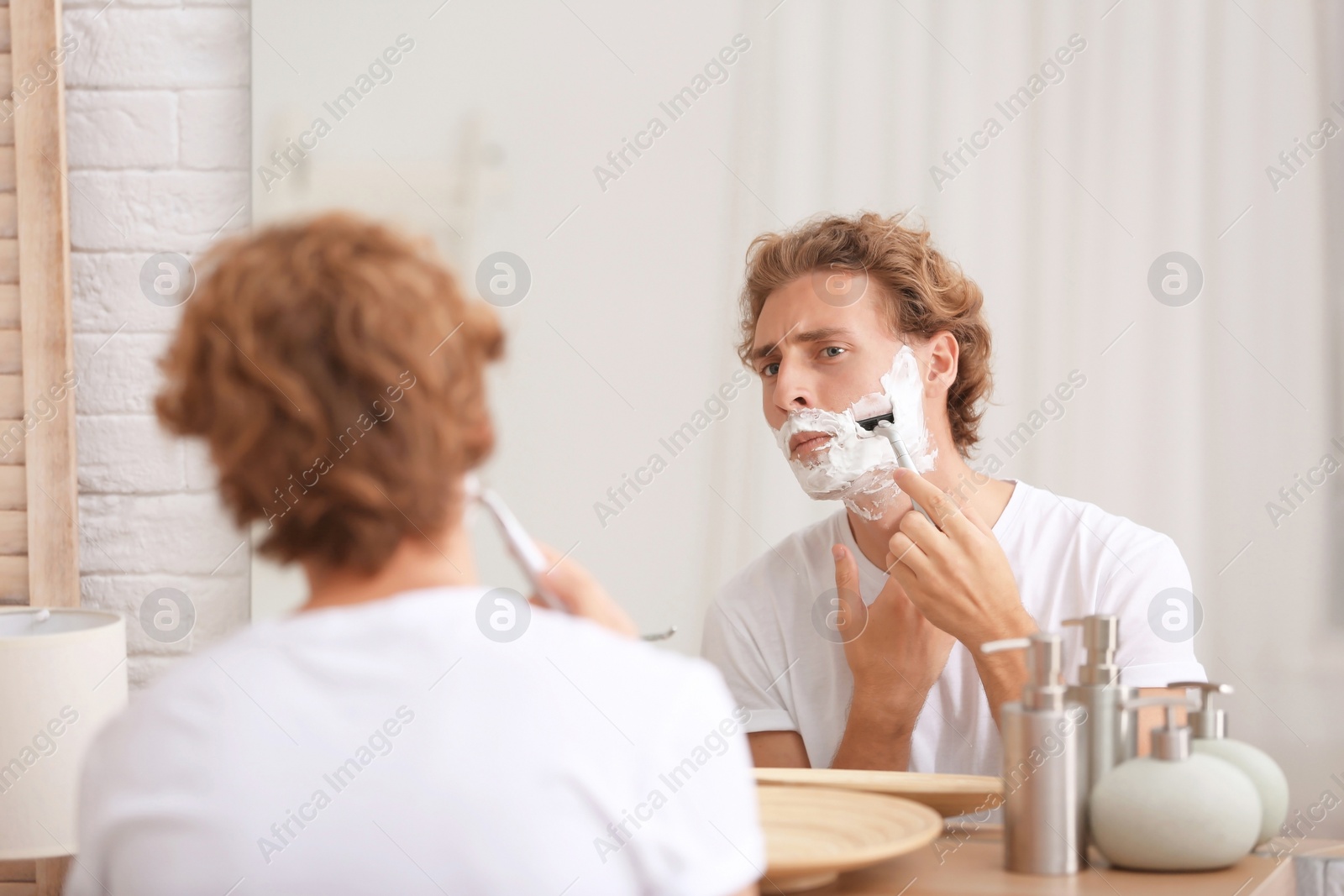 Photo of Young handsome man shaving in bathroom