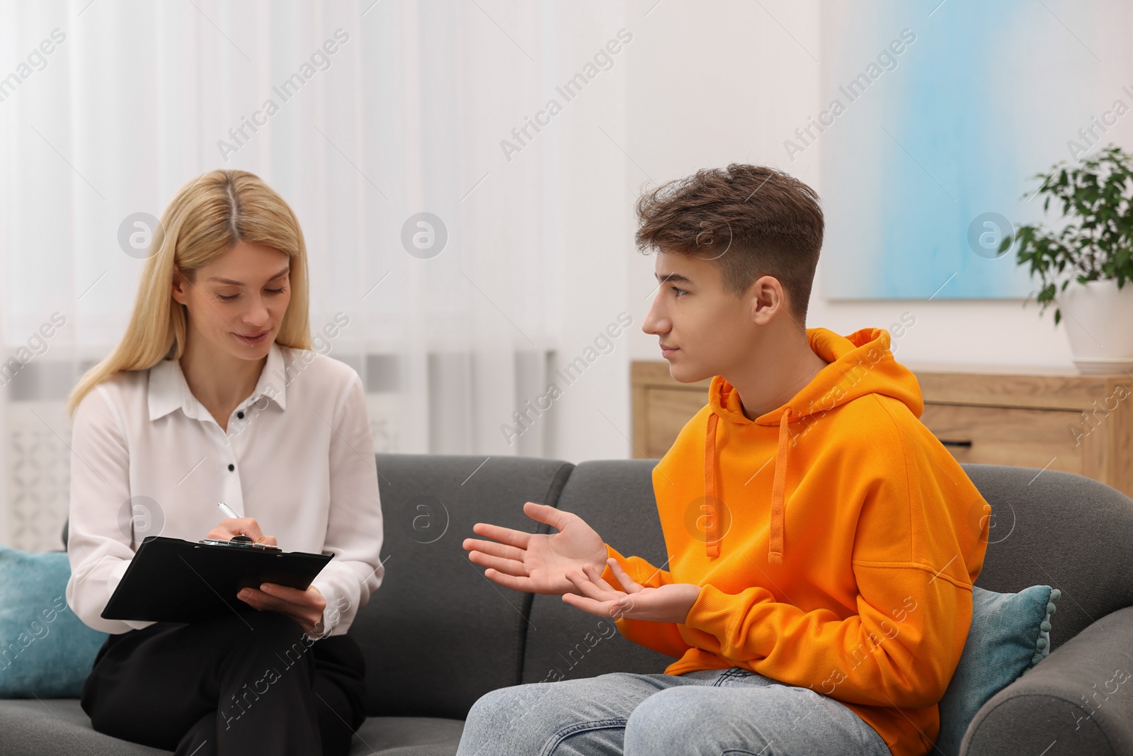 Photo of Psychologist working with teenage boy on sofa in office