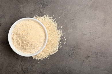 Photo of Bowl with sesame flour and seeds on grey background, top view. Space for text