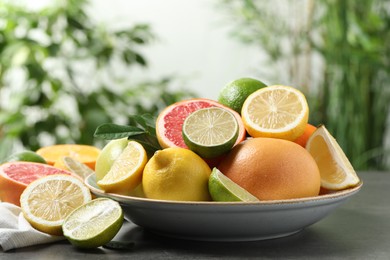 Different fresh citrus fruits on grey table against blurred background, closeup