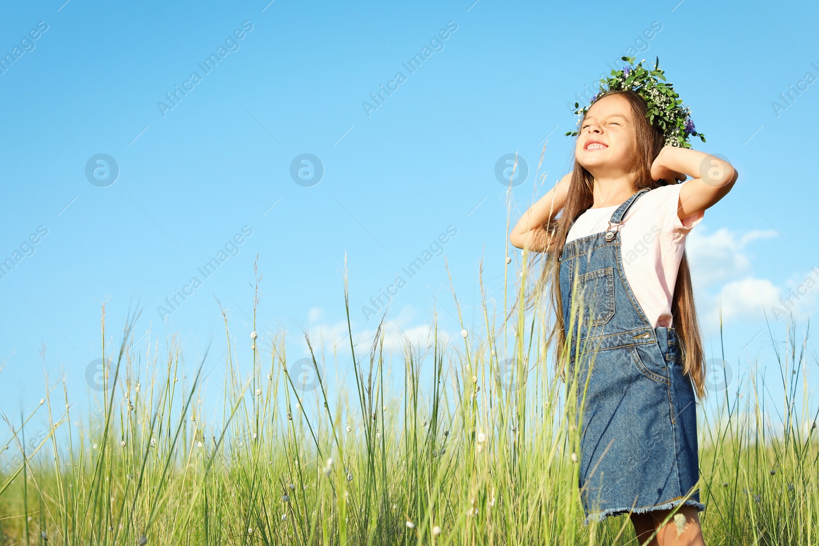 Photo of Cute little girl wearing flower wreath outdoors, space for text. Child spending time in nature