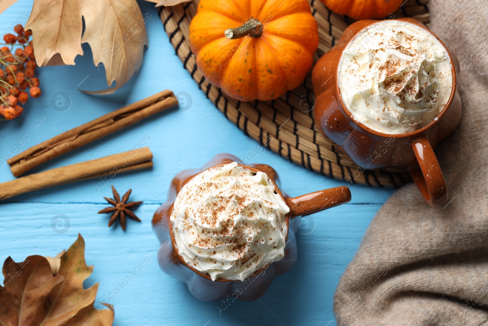 Photo of Flat lay composition with mugs of pumpkin spice latte on light blue wooden table