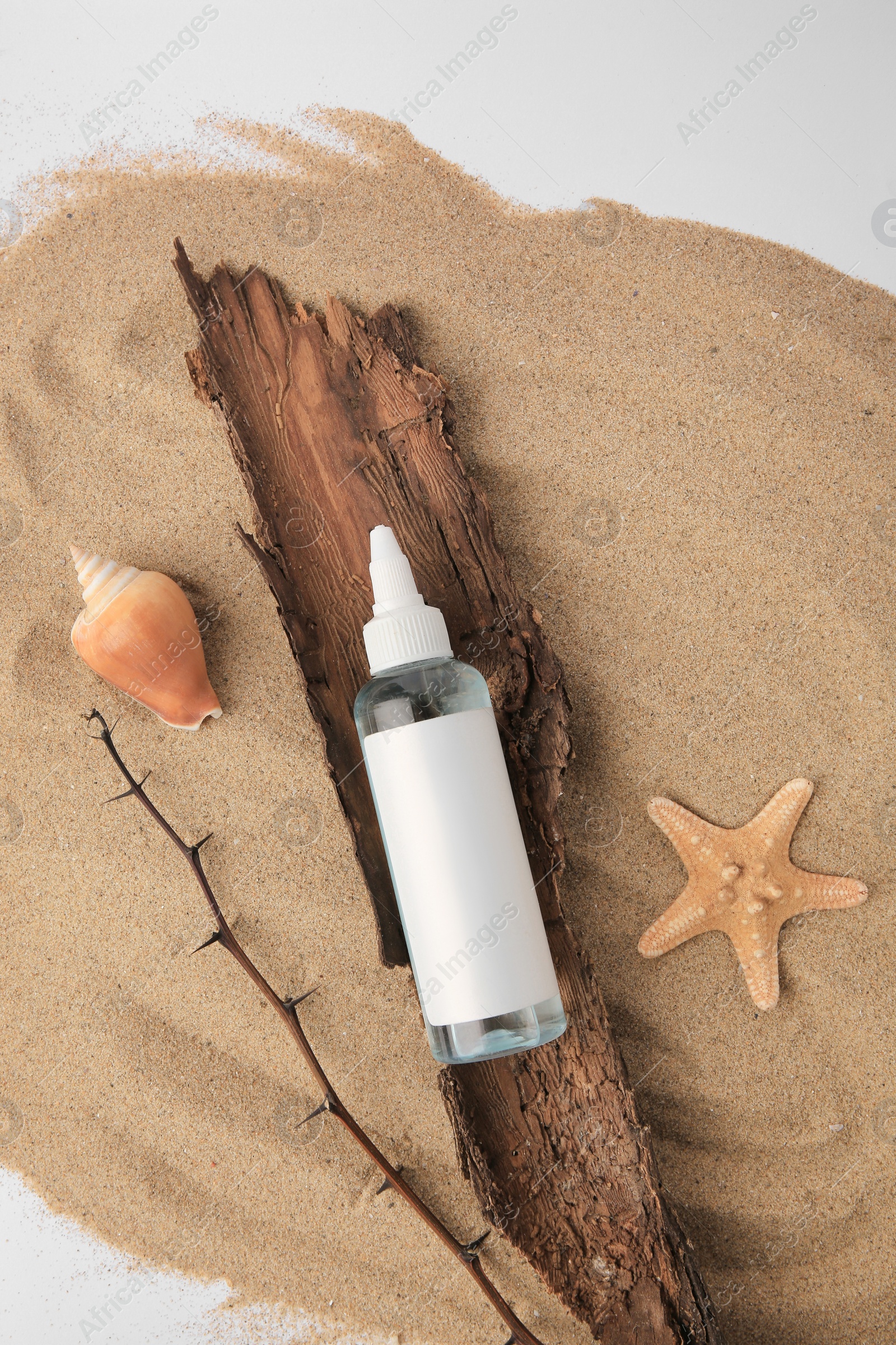 Photo of Flat lay composition with bottle of cream and shells on sand against white background. Cosmetic product