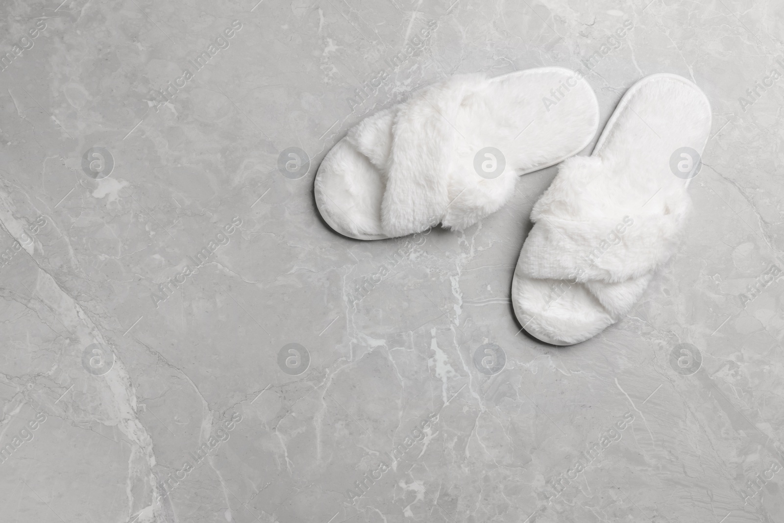 Photo of Pair of soft slippers on grey marble floor, top view. Space for text