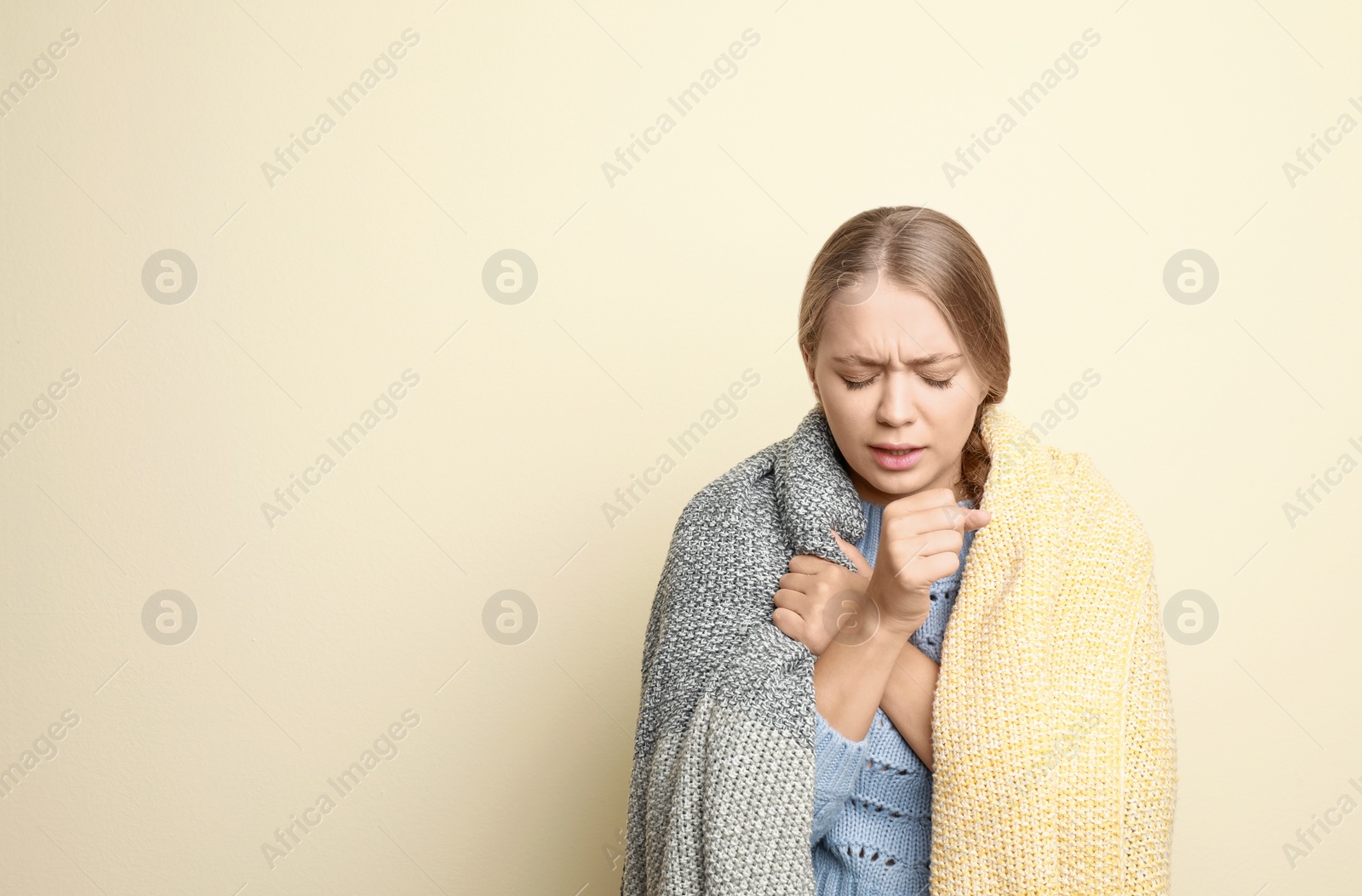 Image of Young woman wrapped in blanket coughing on light background, space for text. Cold symptoms
