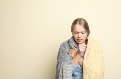 Image of Young woman wrapped in blanket coughing on light background, space for text. Cold symptoms
