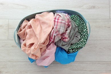 Laundry basket with clothes on white floor, top view