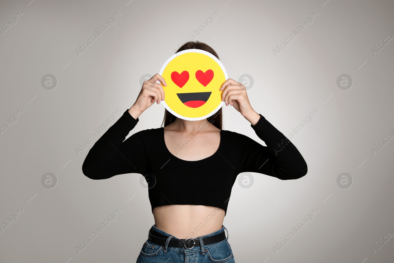 Photo of Woman covering face with heart eyes emoji on grey background