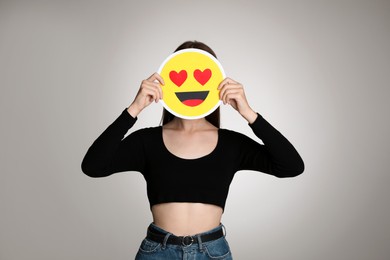 Woman covering face with heart eyes emoji on grey background