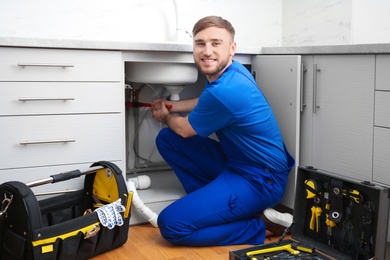 Photo of Professional plumber in uniform fixing kitchen sink