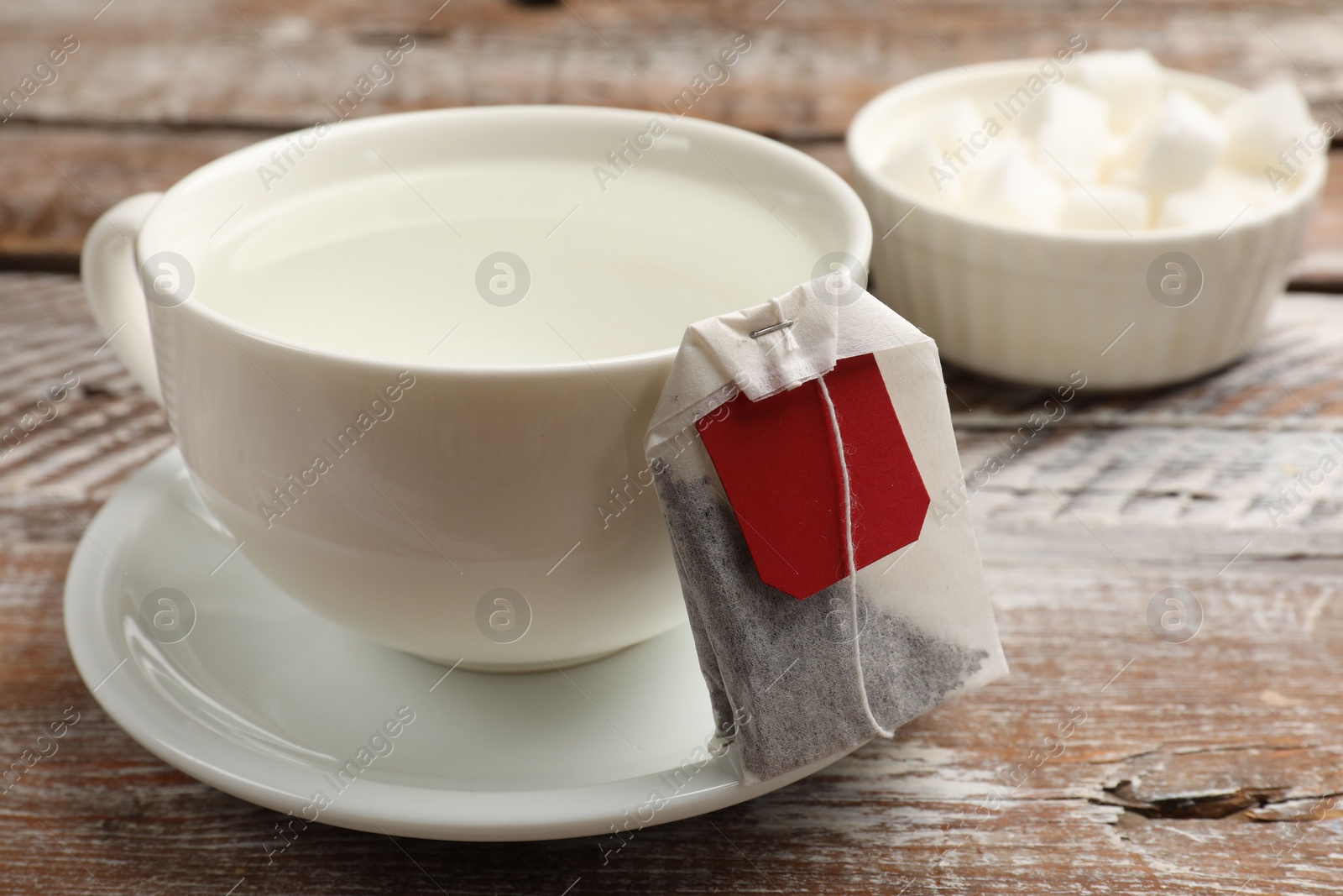 Photo of Tea bag and cup with hot water on wooden rustic table, closeup