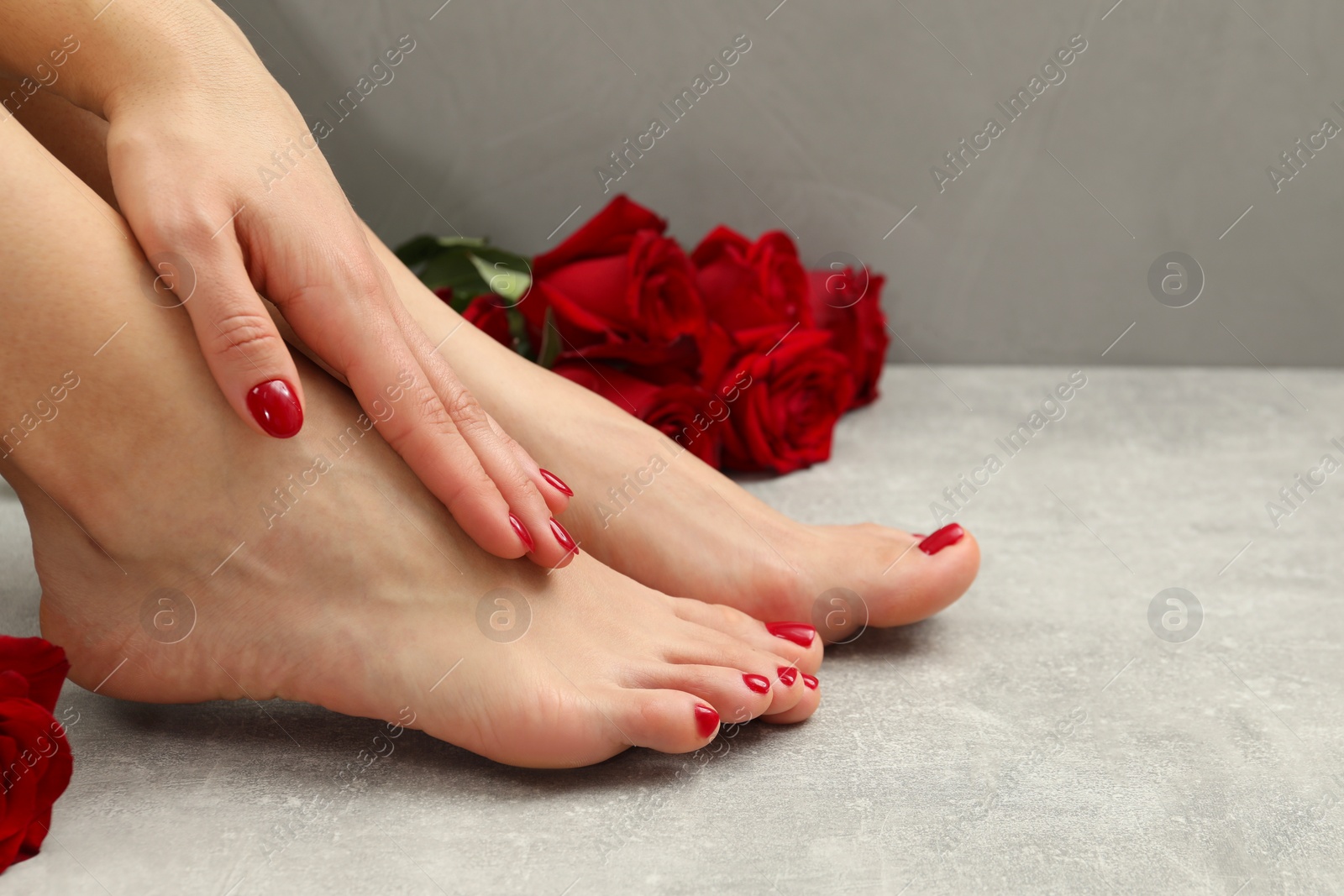 Photo of Woman with stylish red toenails after pedicure procedure and rose flowers on grey textured floor, closeup. Space for text