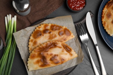 Photo of Delicious fried chebureki with onion served on black table, flat lay