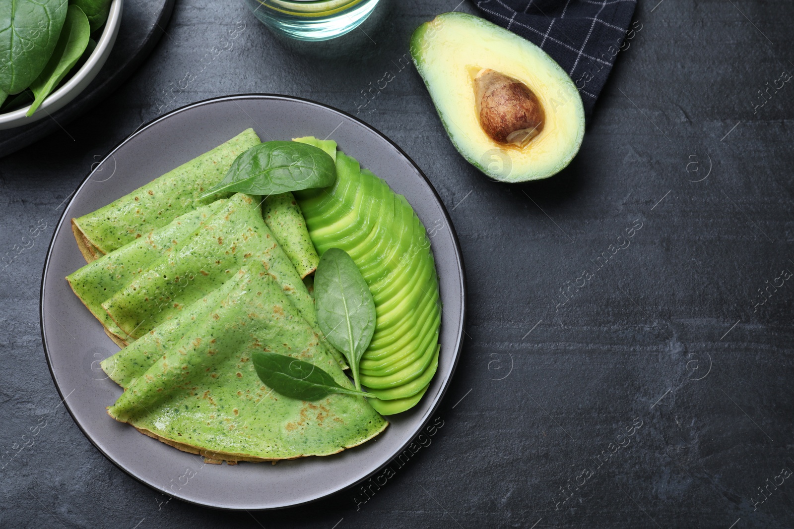 Photo of Delicious spinach crepes with avocado served on black table, flat lay