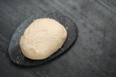 Photo of Fresh yeast dough with flour on black table, top view. Space for text