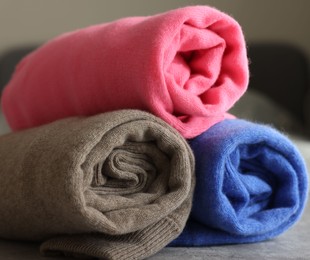 Photo of Rolled color sweaters on gray table, closeup