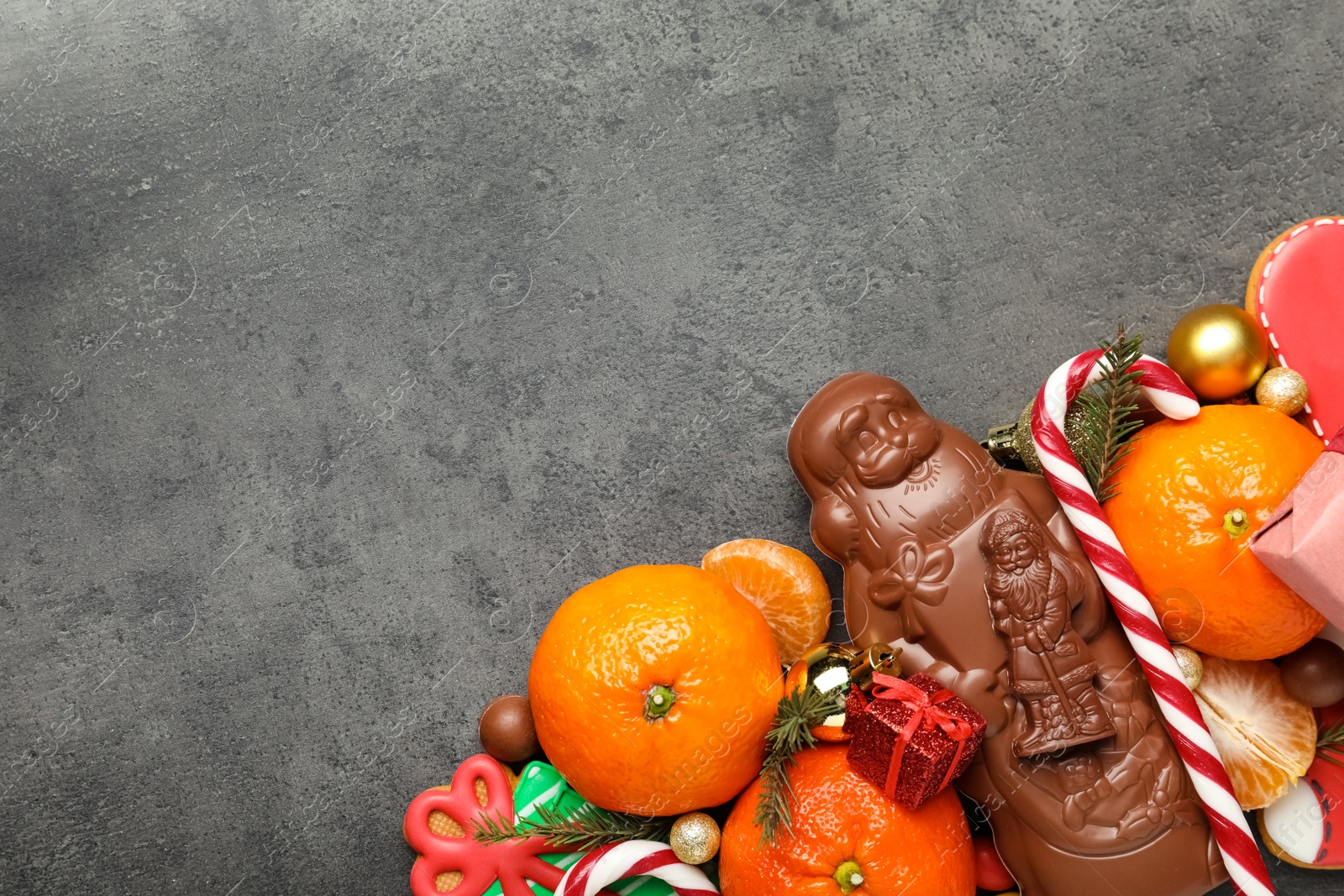 Photo of Flat lay composition with chocolate Santa Claus candies on grey table. Space for text