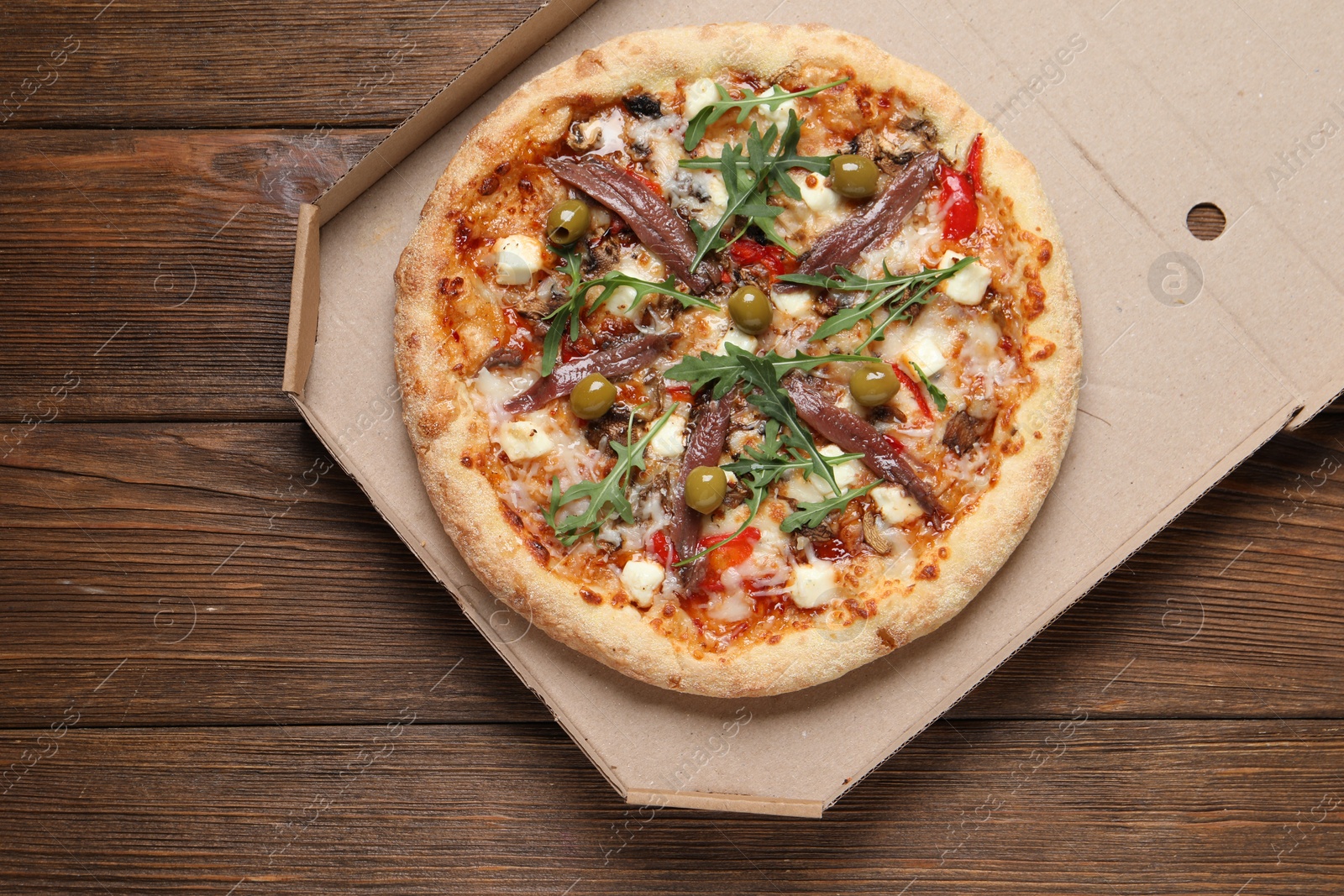 Photo of Tasty pizza with anchovies, arugula and olives on wooden table, top view