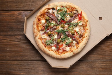 Tasty pizza with anchovies, arugula and olives on wooden table, top view