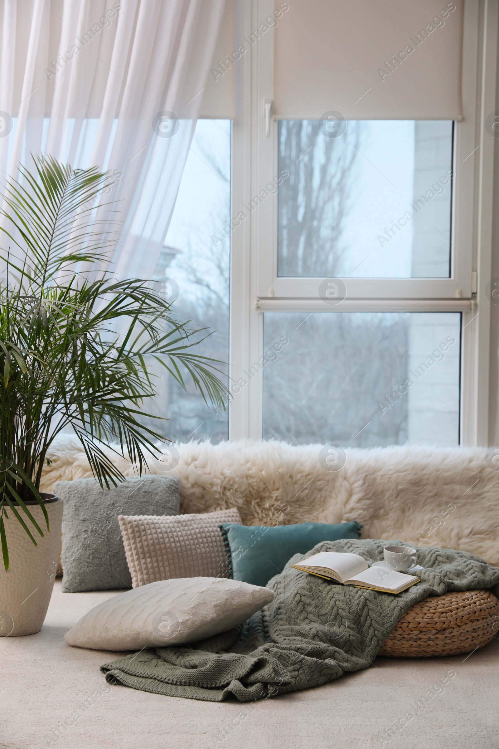 Photo of Comfortable lounge area with faux fur and pillows near window in room