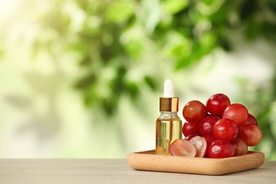 Fresh grapes and bottle of essential oil on wooden table. Space for text