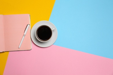 Cup of coffee and notebook with pen on color background, top view. Space for text