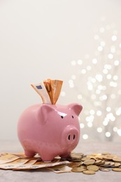 Photo of Piggy bank with euro banknotes and coins on grey table against blurred lights, space for text