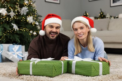Happy couple in Santa hats with Christmas gifts at home