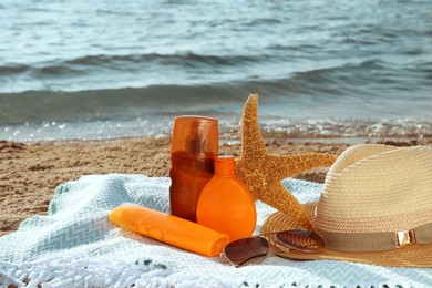 Sun protection products and beach accessories on blanket near sea, space for text