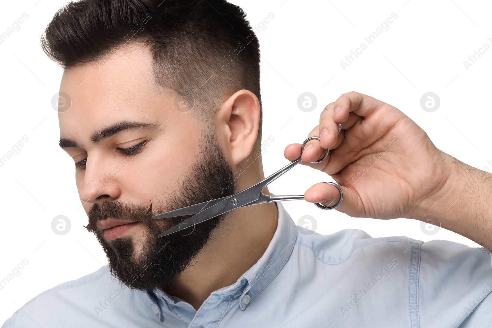 Photo of Handsome young man trimming beard with scissors on white background