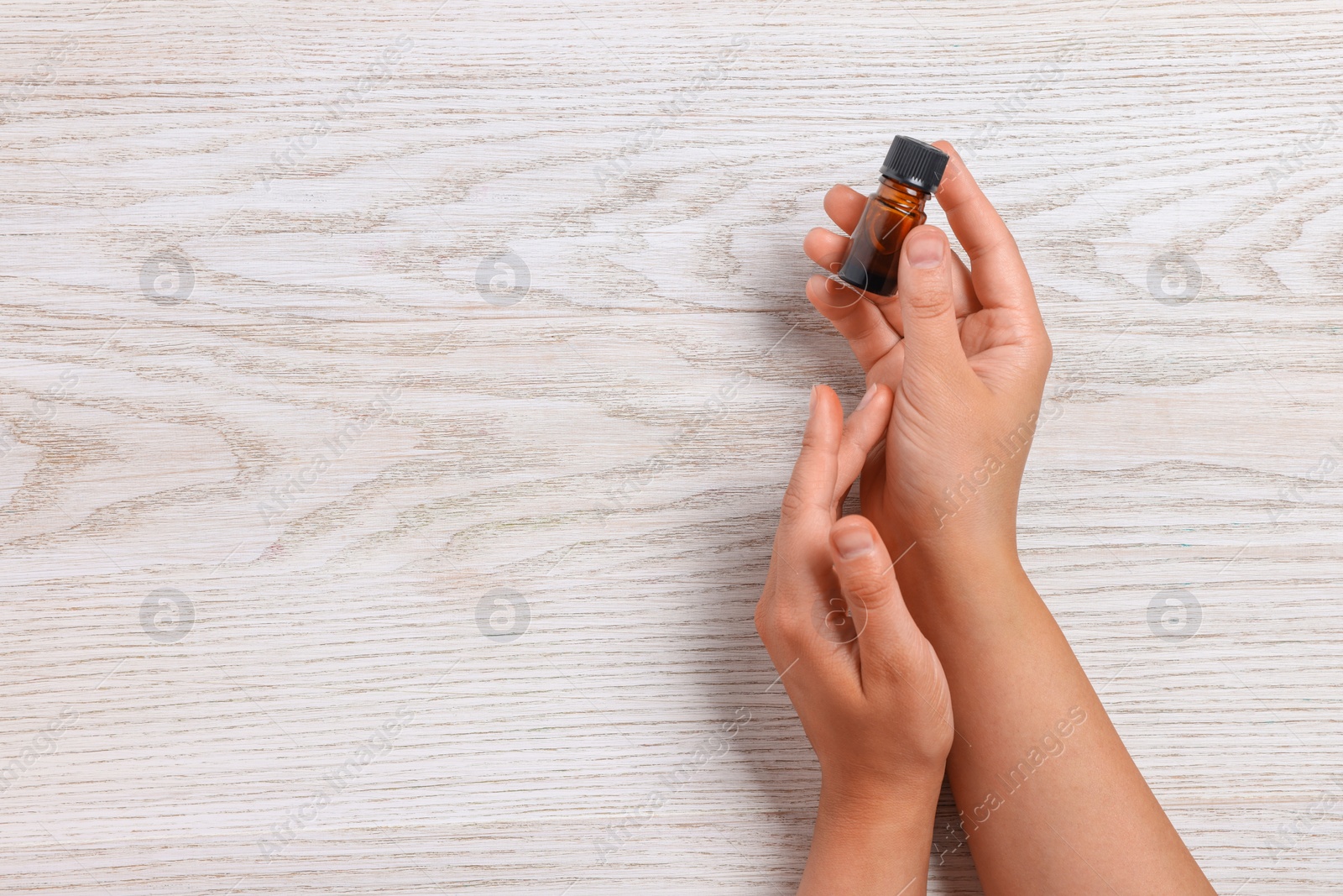 Photo of Woman with bottle of essential oil on wooden background, top view and space for text