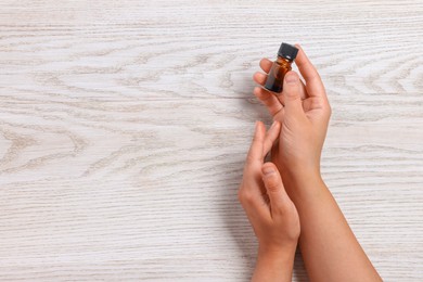 Woman with bottle of essential oil on wooden background, top view and space for text