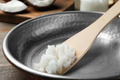 Photo of Frying pan with coconut oil and wooden spatula on wooden table, closeup. Healthy cooking